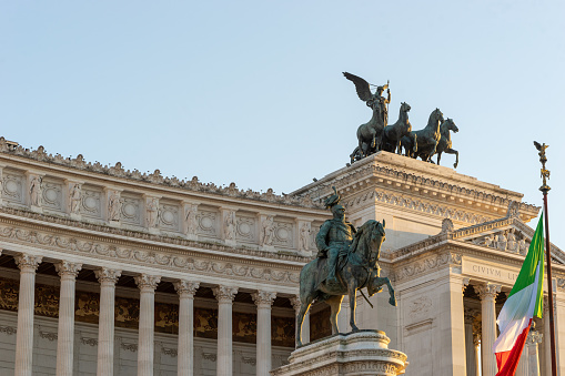 The famous palace of Vittorio Emanuele II in Rome with statue, quadriga on the roof and Italian flag in the evening sun.