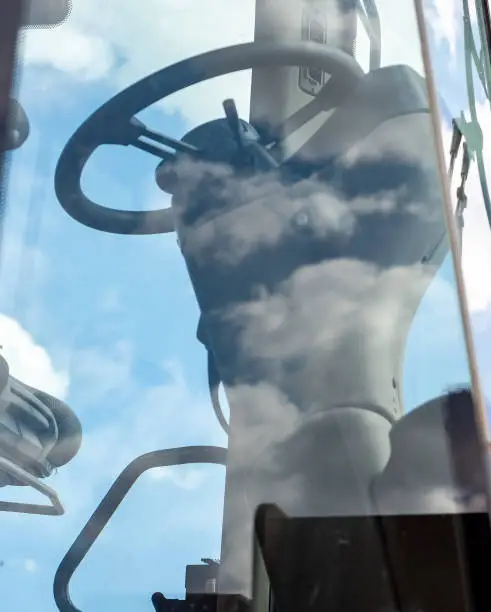 Photo of Steering column, seat and windows of a John Deere construction vehicle with clouds in background and reflecting off windows
