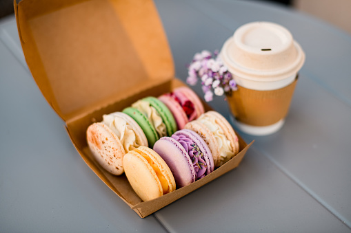 Set of multi-colored macaroons, dried flowers and a paper cup with hot coffee on the table front view