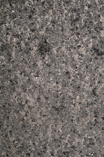 Vertical detailed asphalt texture, uneven rocky wet surface, concrete with sand.