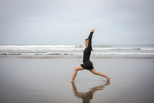 A young, attractive Asian woman is practicing yoga and working out by the beach, embodying the concept of wellness travel experiences.