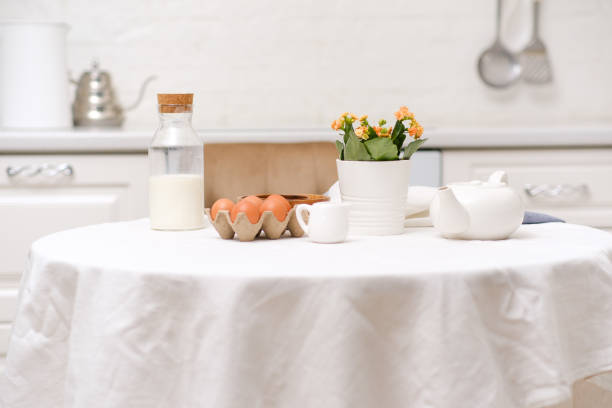 istock Easter celebration concept. Easter eggs, bottle of milk, flowers in white pot, teapot on white table in light kitchen. 2073856072
