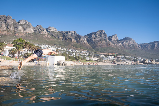 A mid adult male stands on a rock, he is about to take a swim in a cold tidal pool on the coastline near Cape Town.