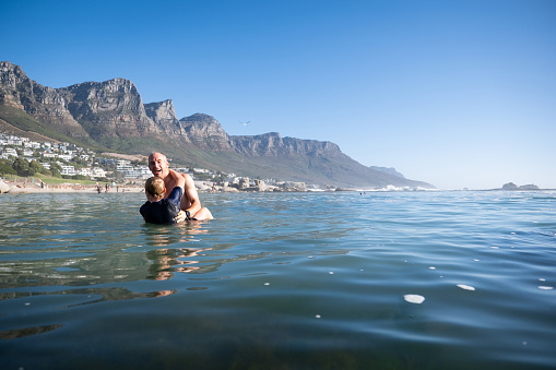 A father has fun wrestling with his teenage son on their summer holiday, they are on vacation at the beach in Cape Town.