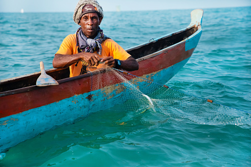 Morondava,Madagascar . 18 october 2023. Malagasy fisherman on homemade wooden old pirogue boat in ocean catches fish with net. selective focus, close-up view from ocean
