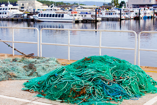 Heap of green ropes tangled on harbor dock, tourboats in the background. O Grove, Pontevedra province, Rías Baixas, Galicia, Spain.