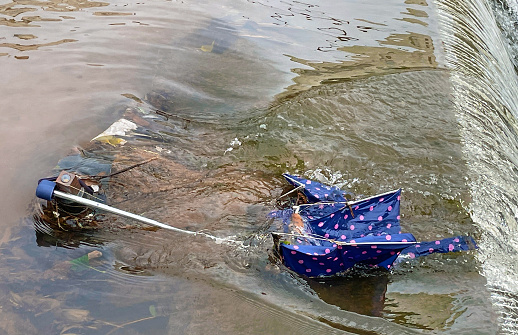 Broken umbrella in fast flowing river after severe storm with copy space