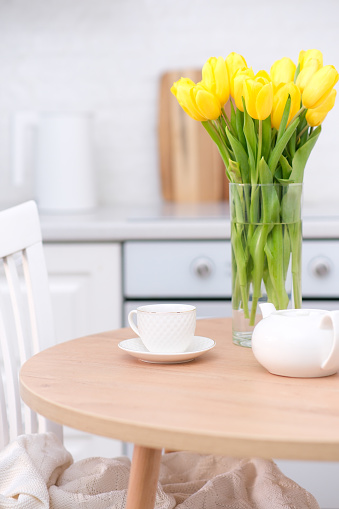 Home kitchen interior.Vase with bouquet of yellow tulips, electric teapot, glass of tea on wooden table. Spring consept. High quality photo