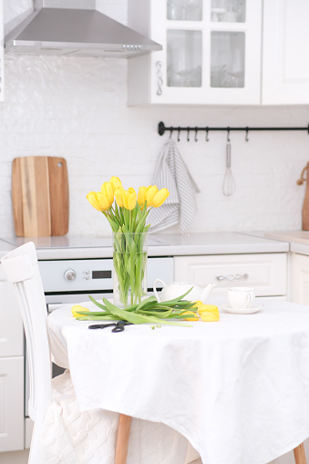 Home kitchen interior.Vase with bouquet of yellow tulips, teapot, sissors on table. Spring consept. High quality photo