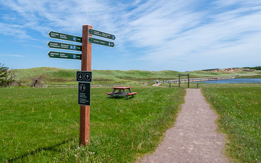 Trail signpost marking the start of the Cavendish Dunelands trail. The footpath crosses a grassy field to a floating boardwalk, near sand dunes.