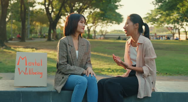Two young Asian women engaged in a cheerful conversation about mental health, seated beside a 