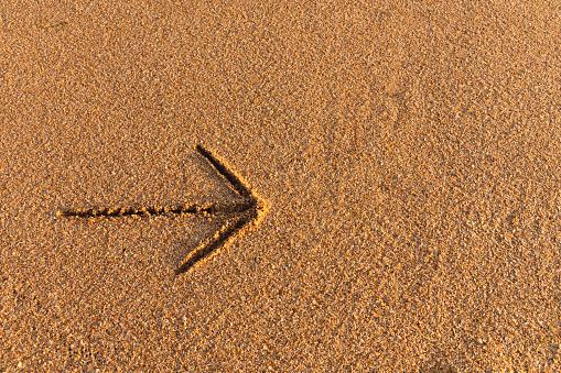 An arrow indicating the direction to the right, an inscription on the sand near the ocean or sea that helps you make a decision. Layout for seaside resort or hotel banner.