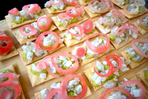 Seafood crackers with avocado and pickled onion topping, arranged on a wooden board.