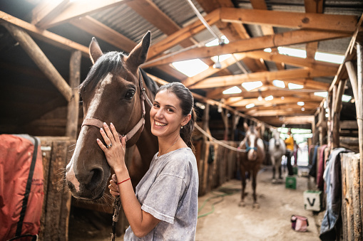 Portrait of a young woman petting horse on a stable
