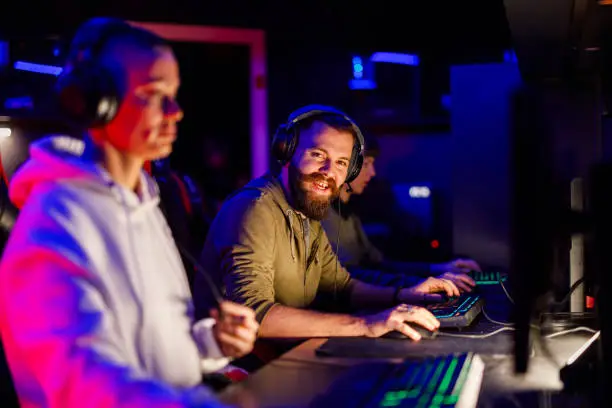 Smiling pro male gamer playing online video games and streaming during tournament in an esports arena or gaming convention in a gameroom. Posing while looking at the camera. Copy space.