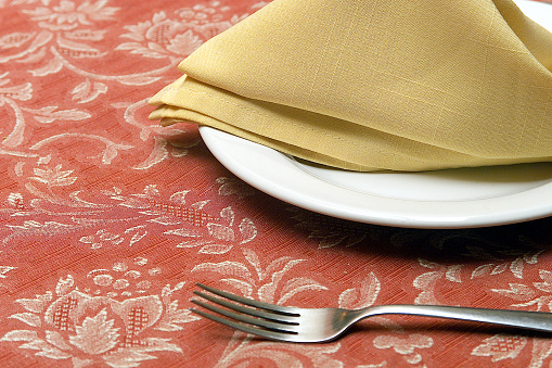 Detail of plate with napkin on flowered tablecloth and a fork, food concept