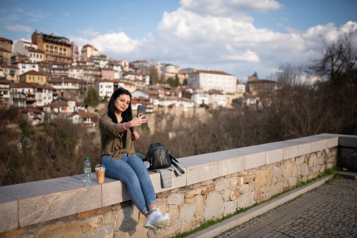 Beaugtiful young woman is taking a selfie with her smart phone while drinking coffee on a nice old town view