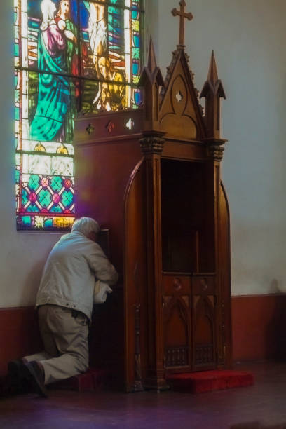 hombre arrodillado en el confesionario - confession booth church forgiveness wood fotografías e imágenes de stock