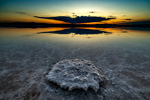 A view of a beautiful sunrise over a pond on a spring or early summer morning with a cloudy sky in the background. Reflection of water and moon