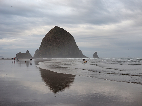 Cannon Beach, Oregon - 9/30/2018: Small group of people enjoy stroll around Haystack Rock at extreme low tide under dramatic autumn cloudscape.