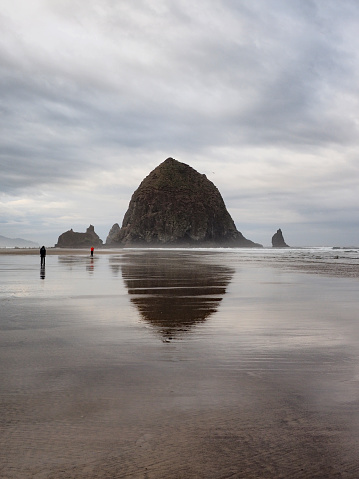 Cannon Beach, Oregon - 9/30/2018: Small group of people enjoy stroll around Haystack Rock at extreme low tide under dramatic autumn cloudscape.
