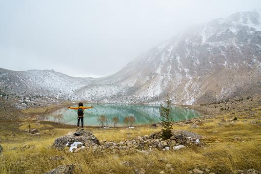 Adventurous traveler poses with arms outstretched in front of a lake in the middle of the mountains