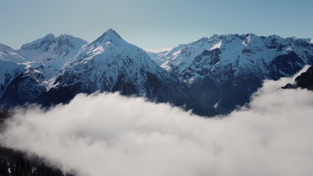 Drone video flying through the clouds towards a snowy mountain range