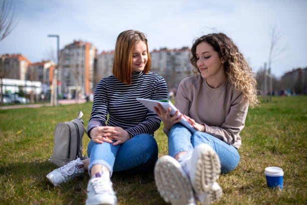 istock Two female students studying together while sitting on a grass at public park 2074270964