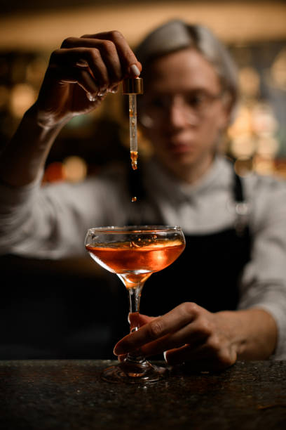 istock Female bartender adds a drink drop by drop to a cocktail glass with a dropper 2074278277