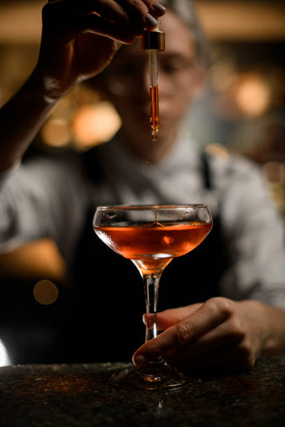 istock Female bartender adds a drink drop by drop to a cocktail glass with a dropper on a blurred background 2074278791