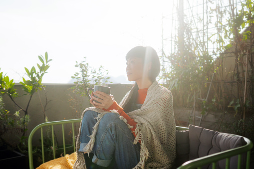 Photo of a Japanese woman enjoying early morning coffee on the balcony of a loft apartment