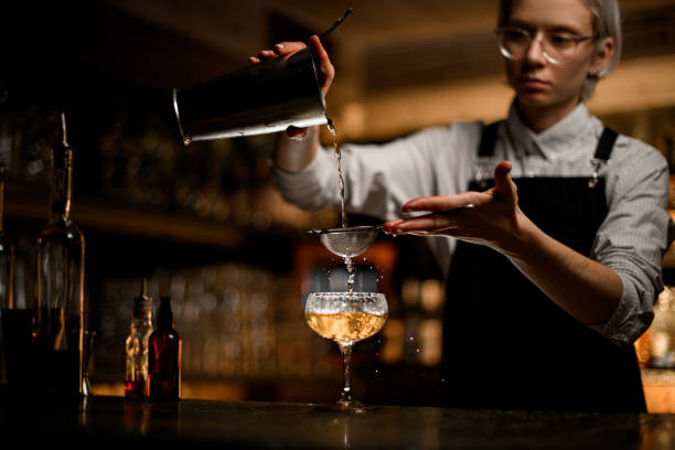 istock Female bartender pours a clear liquid from a metal beaker into a glass with a sieve 2074280366