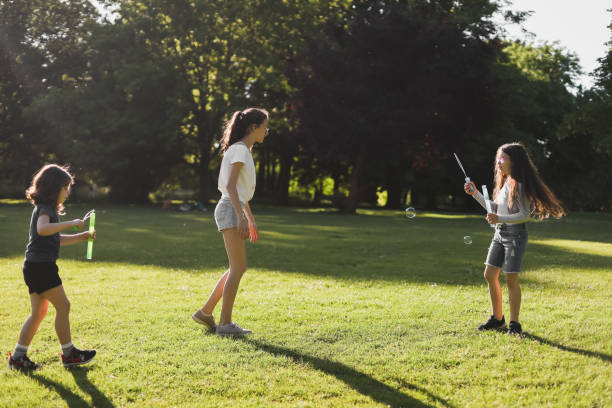 portrait of three girls-sisters playing and blowing soap bubbles in the park. - outdoors playing family spring imagens e fotografias de stock