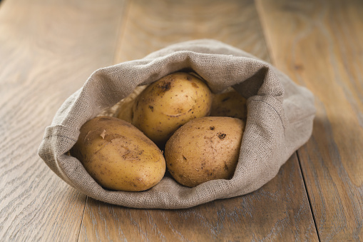 fresh raw potatoes in sack on wood background, shallow focus