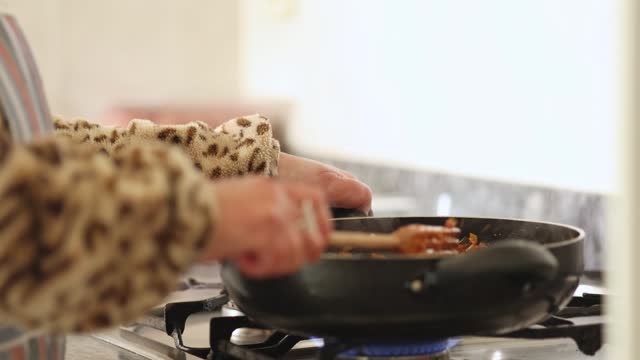 woman at home cooking food in a frying pan simmering on the stoves