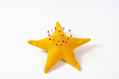 Yellow star-shaped pincushion with colored pins pinned on a white background.