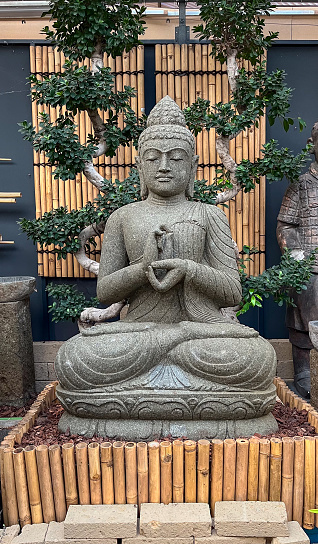 Stone Buddha figure sitting in an indoor garden with a background of oriental trees and bamboo