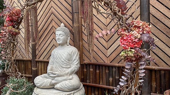 Stone Buddha figure sitting in an indoor garden with a background of oriental trees and bamboo
