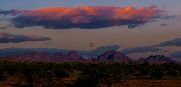 Arizona desert in  springtime with the moon setting and the sun rising with colorful clouds and mountains