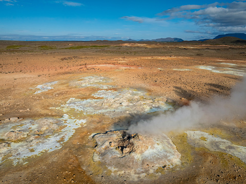Wide shot of flat green geothermal fields near yellow rhyolite mountain, beautiful colorful volcanic landscape in Iceland, aerial view.