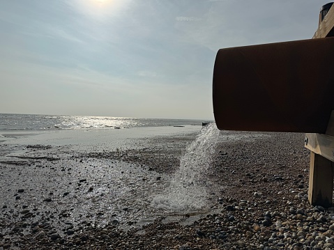 A large pipe discharging something on to the beach