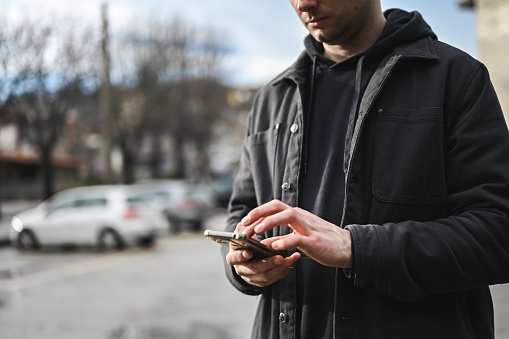 Midsection of a young man with mobile phone on a city parking.