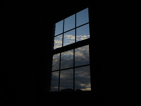 The sky photographed through a dark window with dramatic clouds and bright colors as the sun sets.
