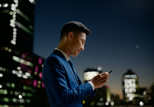 Business, man and reading phone at night in city for communication, email and text message on rooftop. Entrepreneur, asian person and smartphone for internet scroll, social media and mobile chat