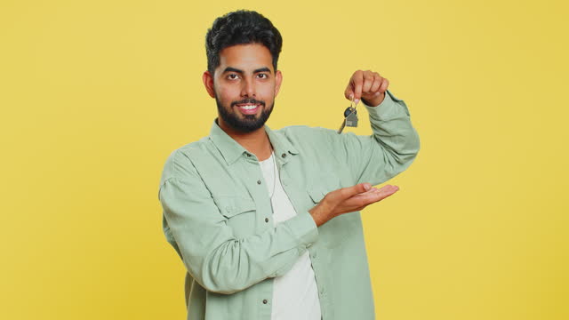 Indian young man real estate agent showing keys of new home house apartment, buying renting property