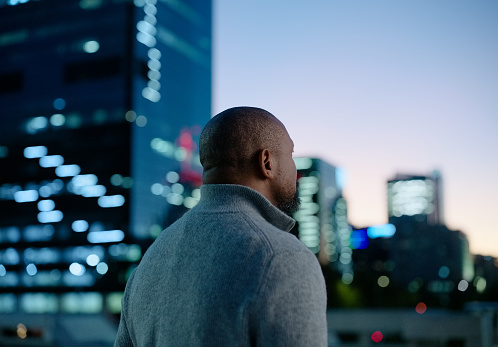 Businessman, thinking and night city with buildings or career opportunity thoughts of future, planning or goals. Male person, back and bokeh lights in downtown London or vision, rooftop or balcony