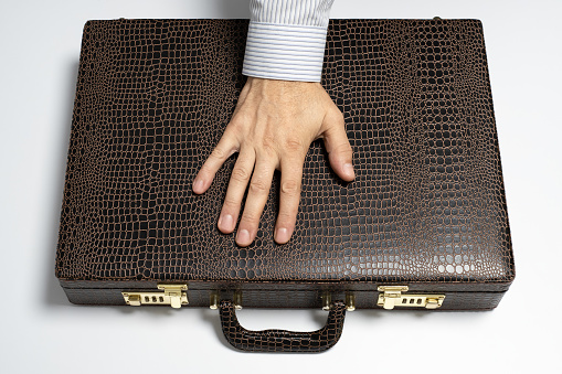 A man's hand on a brown briefcase with textured material, symbolizing professionalism in business or the concept of huge bribery.