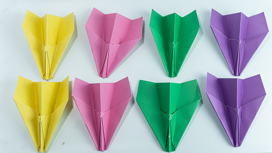 Paper airplanes lined up in pink, purple, green, and yellow isolated on a white background