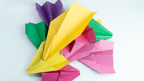Pile of pink, purple, green and yellow paper airplanes isolated on white background
