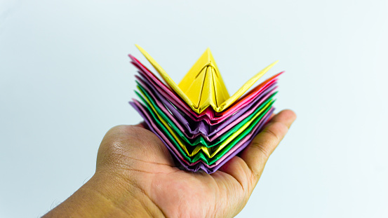 Stacked paper airplanes in pink, purple, green and yellow in hand isolated on white background